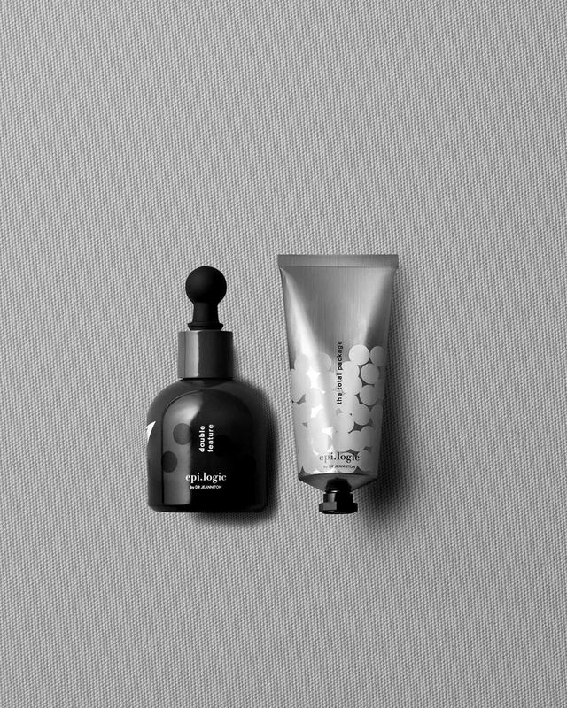 An Epi.Logic serum bottle and cream tube laid flat on a grey surface